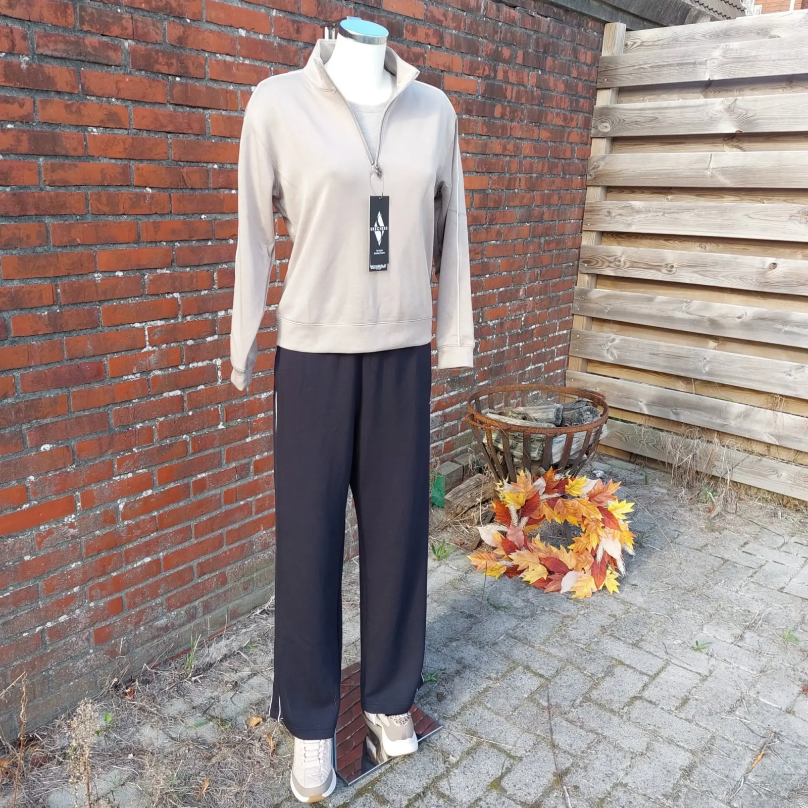 Skechers-outfit: taupe trui met korte rits, zwarte broek met witte bies en sneakers
